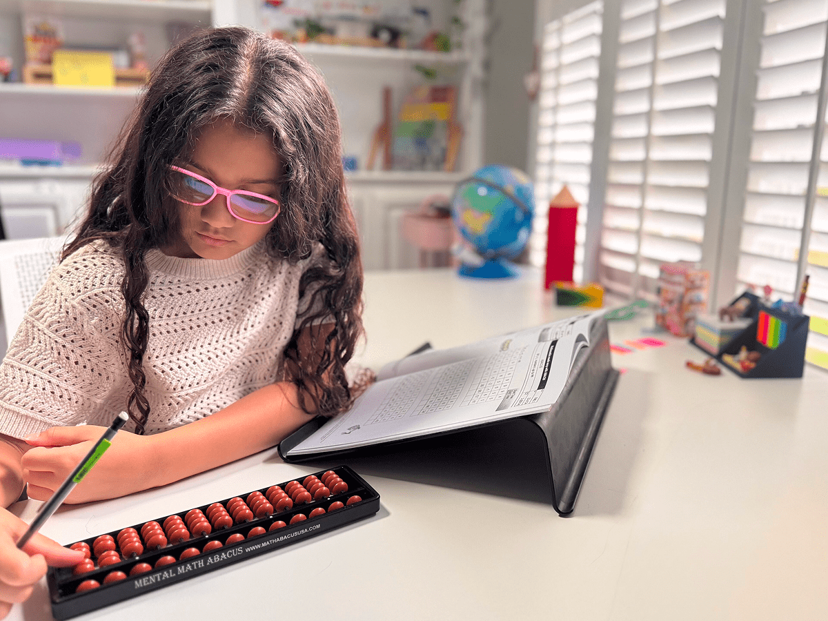 Girl using abacus and workbook at desk.