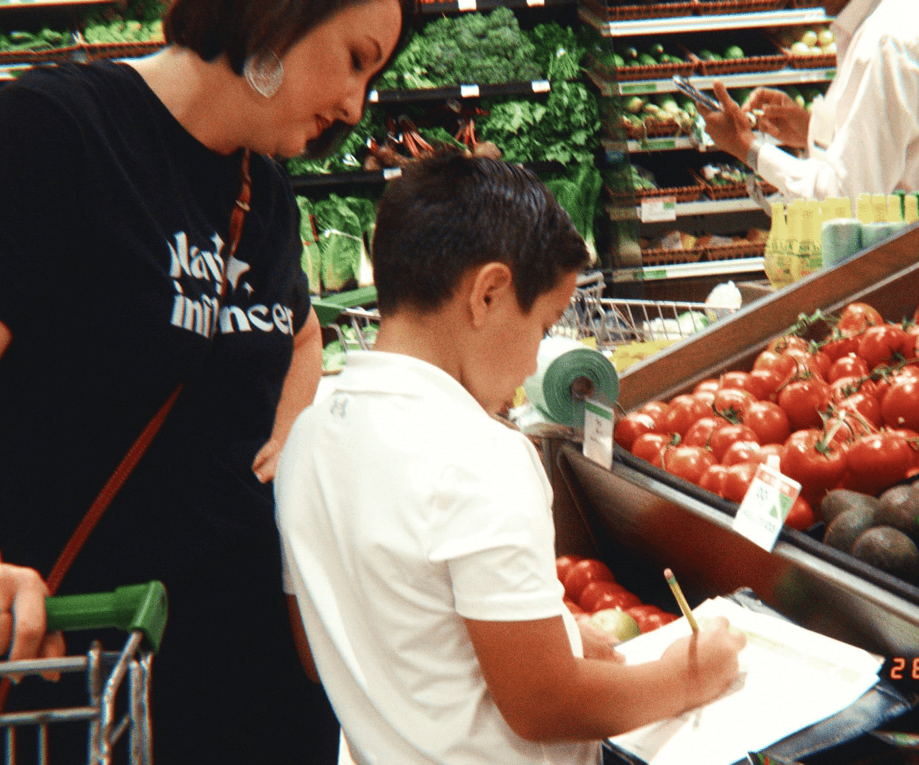Child writing in grocery store produce section.